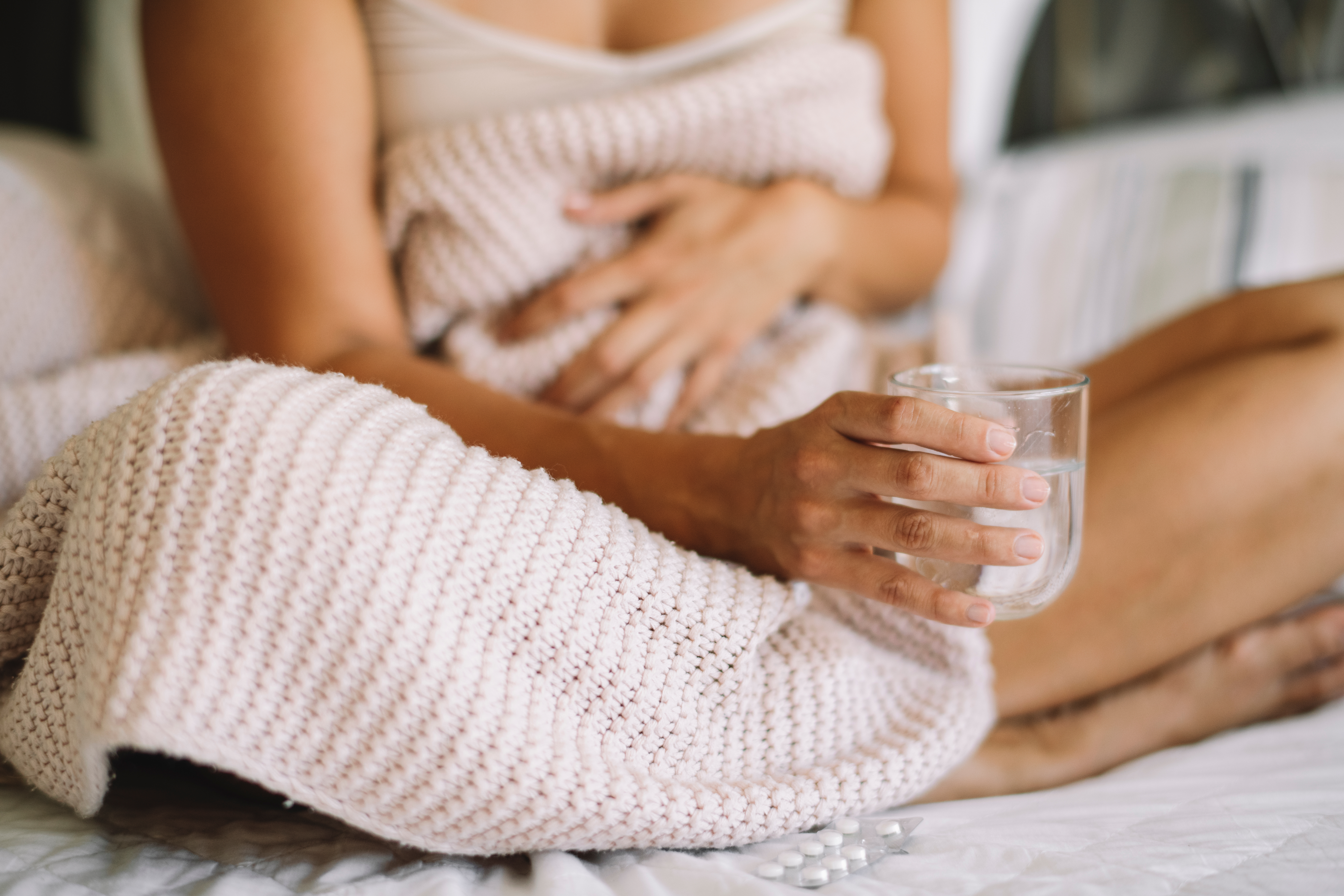Eine Frau mit Blasenentzündung während ihrer Periode sitzt im Bett mit einem Glas in der Hand.