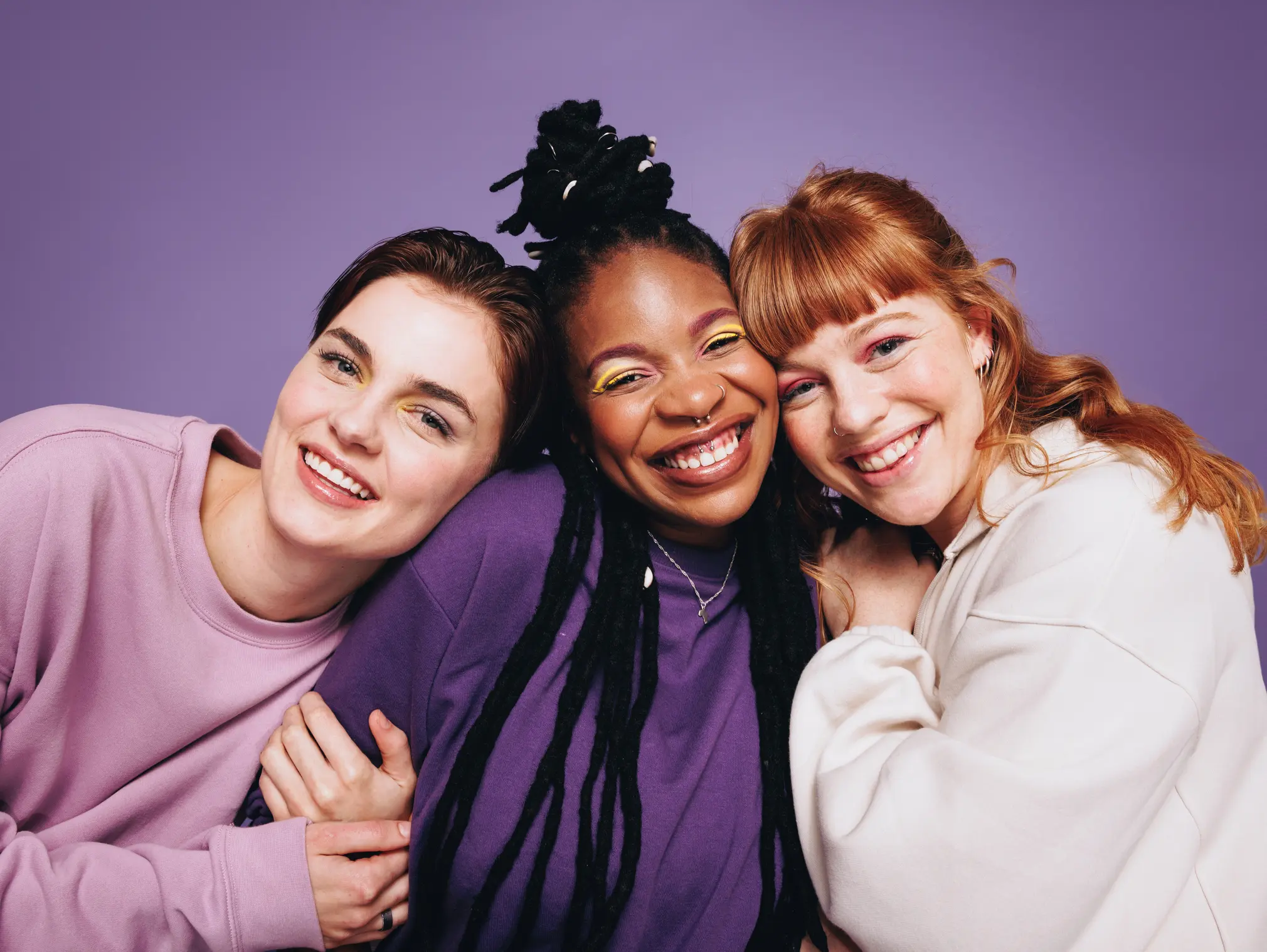 Drei Frauen halten sich in den Armen und lachen in die Kamera.