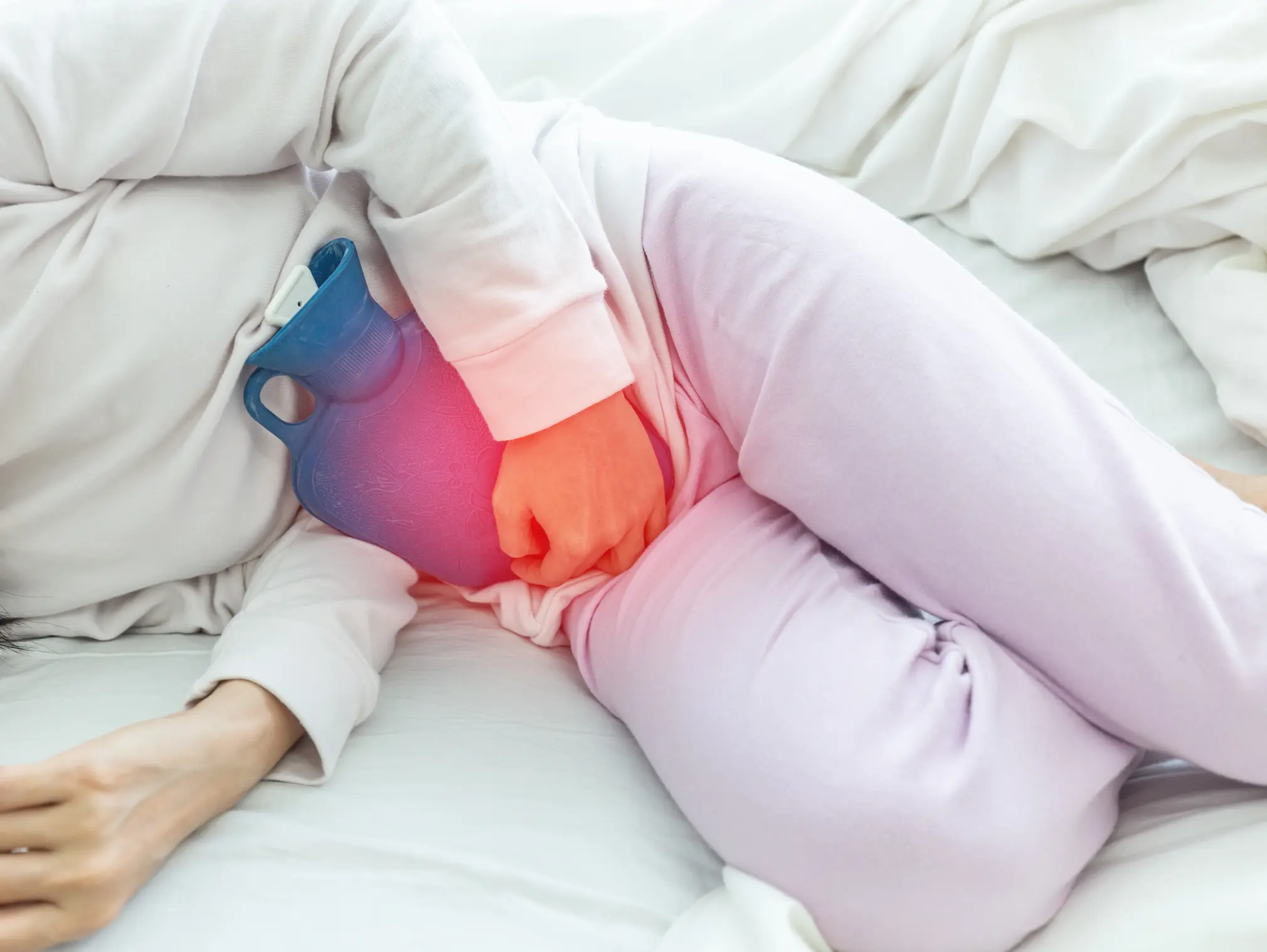 Frau mit chronischer Blasenentzündung liegt mit Wärmflasche im Bett.