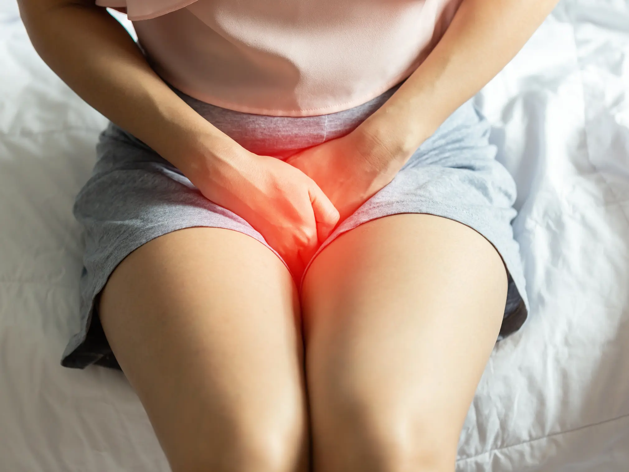 Frau kneift die Beine zusammen und hält ihre Hände vor den Intimbereich, denn die Symptome ihrer Blasenentzündung sind sehr unangenehm.