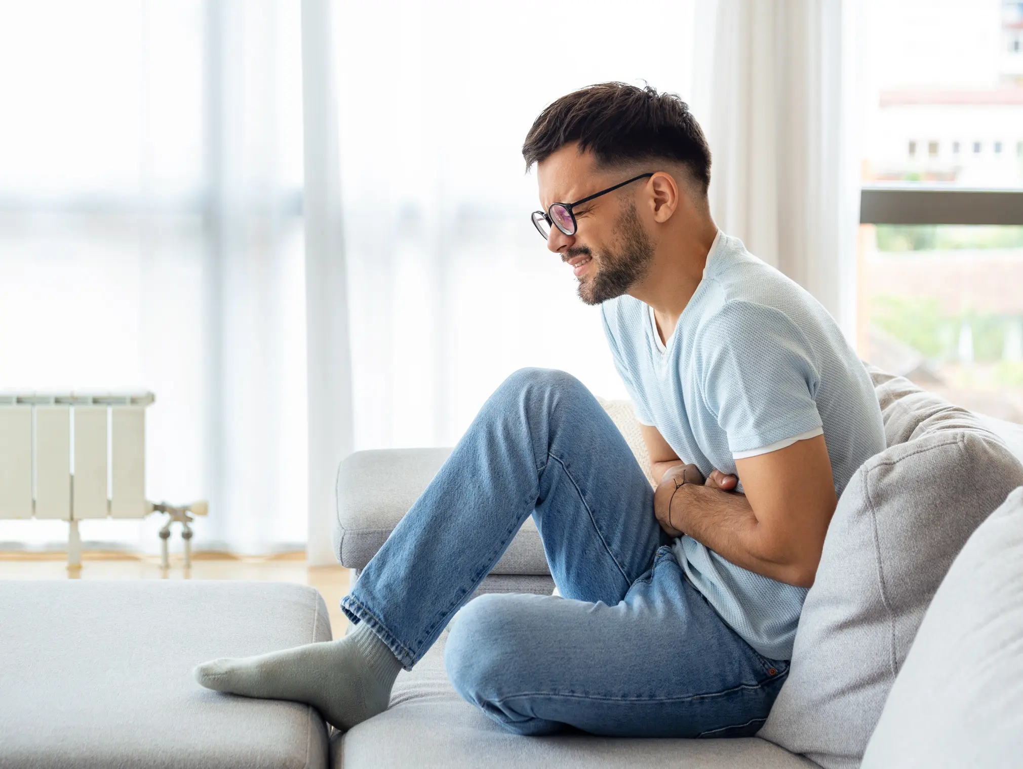 Mann hält sich vor Schmerzen den Unterbauch – ein Symptom bei Harnsteinen.