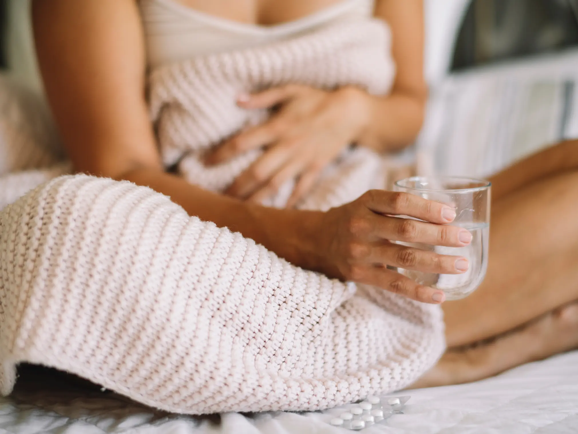 Eine Frau mit Blasenentzündung während ihrer Periode sitzt im Bett mit einem Glas in der Hand.