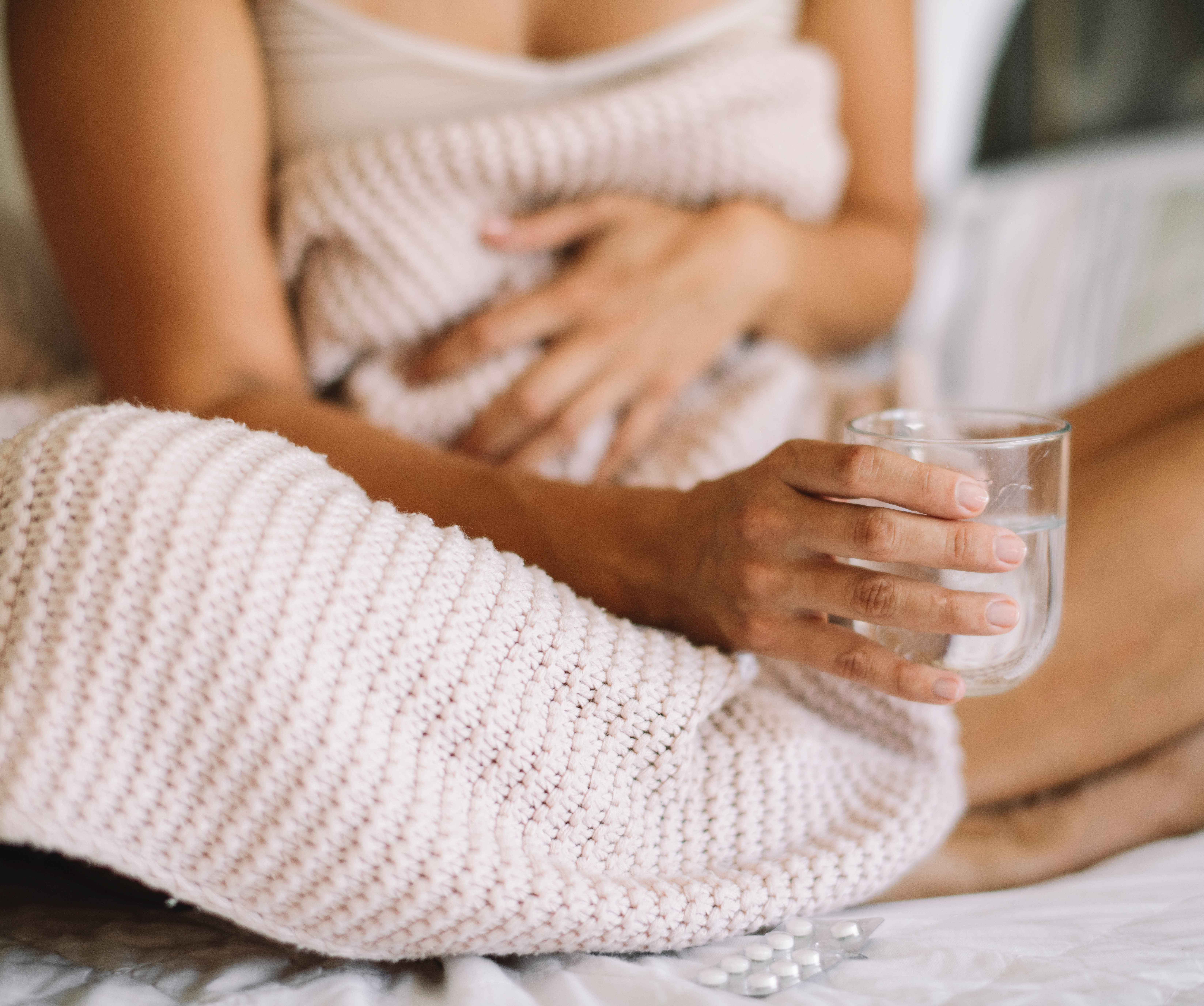 Eine Frau mit Blasenentzündung während ihrer Periode sitzt im Bett mit einem Glas in der Hand.